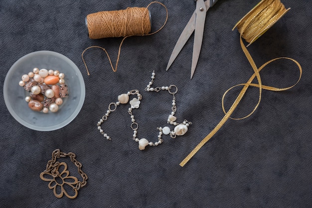 Bracciale realizzato con rocchetto di filo; perline; forbice e nastro dorato su sfondo nero con texture