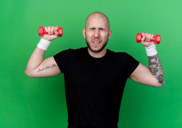 Braccialetto da portare da portare del giovane sportivo teso che si esercita con i dumbbells isolati sul verde