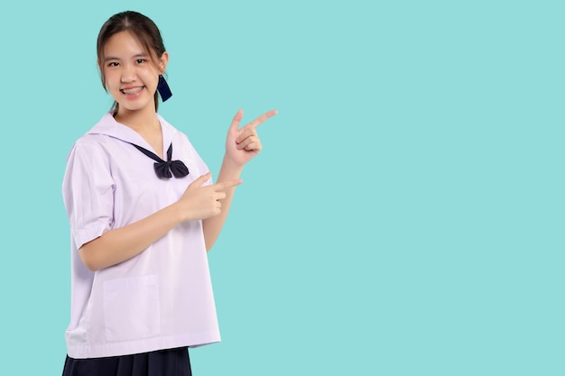 Bretelle felici Studentessa asiatica in uniforme scolastica con il dito puntato su sfondo pastello isolato