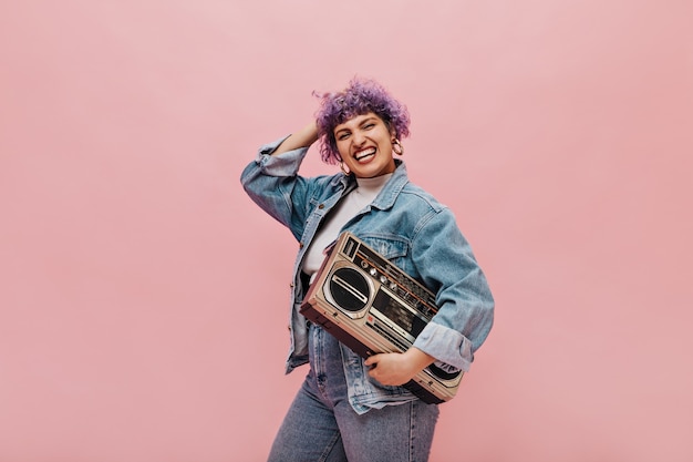 Brillante donna dai capelli corti con enormi orecchini rotondi e ampia giacca tiene il registratore nel fiume e continua a ridere.