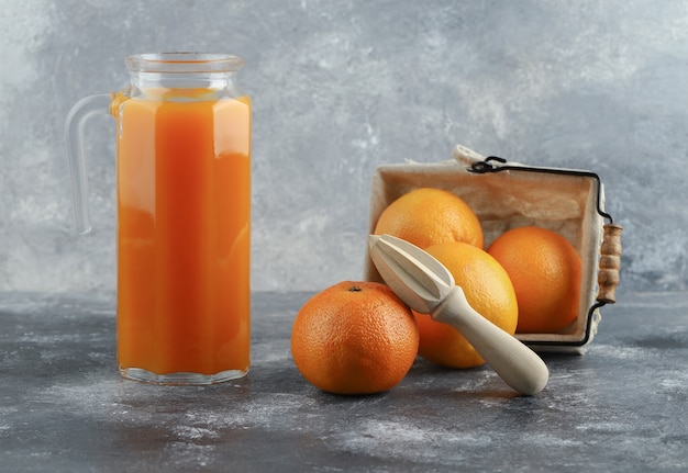 Brocca di succo e cesto di arance sul tavolo di marmo.