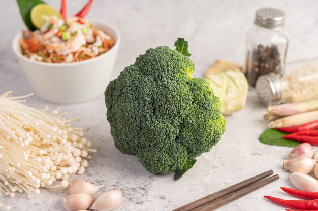 Broccoli, ago d'oro fungo, bacchette, aglio e peperoncini rossi su un pavimento di cemento bianco