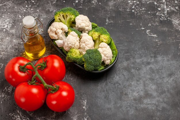 Broccoli e cavolfiori di vista frontale sull'olio dei pomodori del piatto sullo spazio libero del fondo scuro