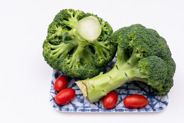 Broccoli freschi con il pomodoro ciliegia in piatto su superficie bianca