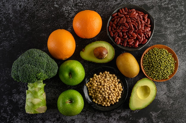 Broccoli, mela, arancia, kiwi, legumi e avocado su un pavimento di cemento nero.