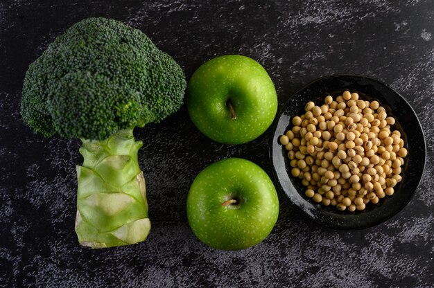 Broccoli, mela e fagioli di soia su un pavimento di cemento nero.