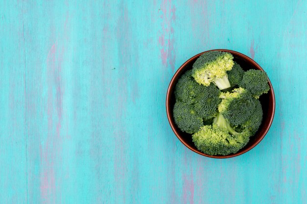 Broccoli verdi freschi di vista superiore sul piatto su superficie di legno blu