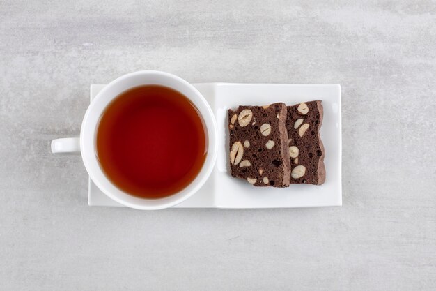 Brownie al cioccolato fatti in casa e una tazza di tè su un piatto, sul tavolo di marmo.