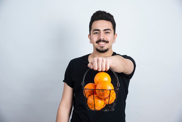 Bruna modello uomo in piedi e tenendo il cesto metallico con frutti arancioni.