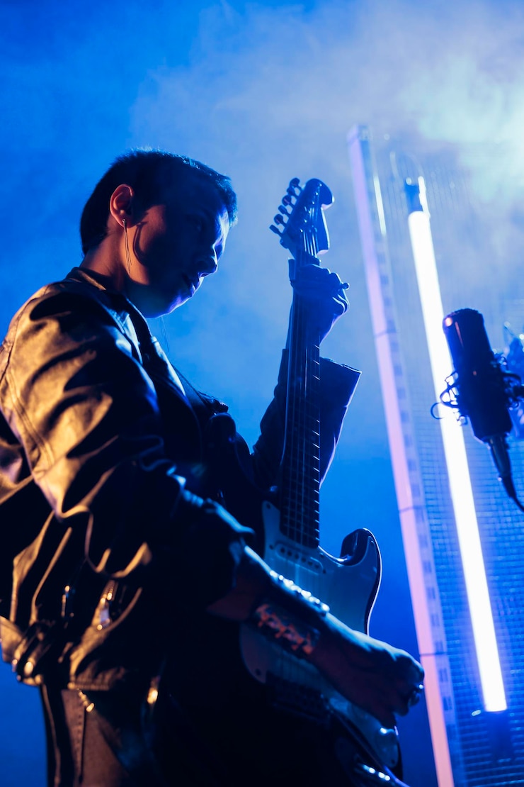 Foto gratuito bruna rockstar con i capelli corti che tiene la chitarra elettrica che suona musica rock preparando una canzone pesante da esibirsi al concerto grunge. chitarrista donna in giacca di pelle che regola lo strumento elettrico