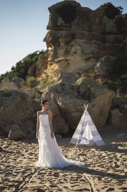 Bruna sposa caucasica in posa sulla spiaggia davanti a una tenda bianca