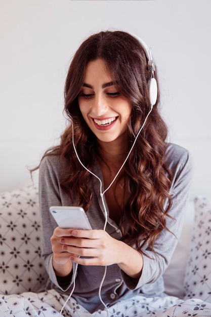 Brunette sorridente che sceglie musica sullo smartphone
