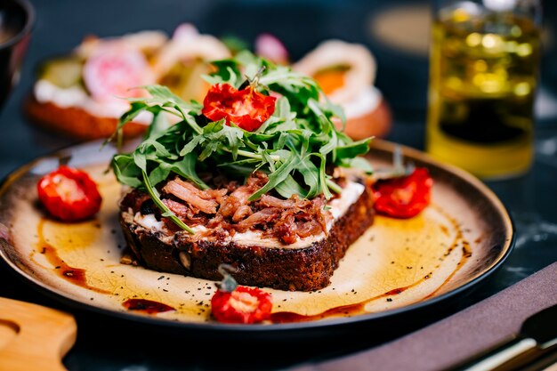 Bruschetta con la vista laterale della salsa di crema di formaggio della rucola del pomodoro della carne