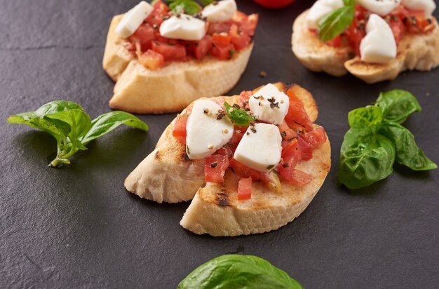 Bruschetta con pomodori, mozzarella e basilico su un tagliere. Antipasto o spuntino tradizionale italiano, antipasto. Bruschetta con insalata caprese. Vista dall'alto con copia spazio. Lay piatto.