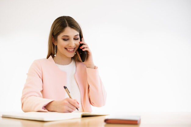 Buinesswoman con candido sorriso in chat per telefono e godersi la pausa caffè nella caffetteria. Indossare giacca casual rosa maglione bianco