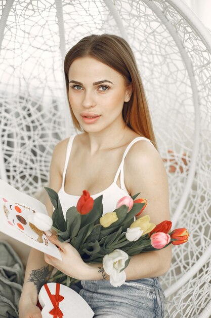 Buon San Valentino. Giovane donna seduta su una sedia con tulipani e biglietto di auguri.