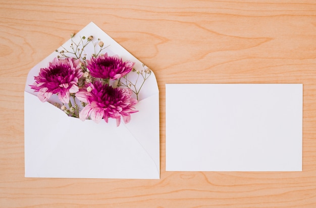 Busta bianca con fiori e carta su fondo strutturato in legno