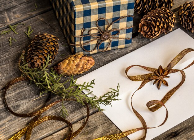 Busta bianca sulla parete di legno con pigne e regalo di Natale