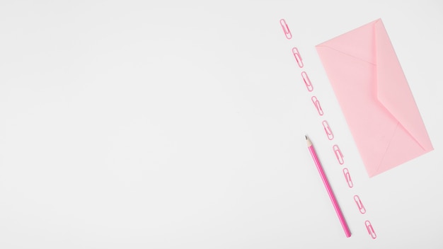 Busta rosa e fila di graffette e matita su sfondo bianco