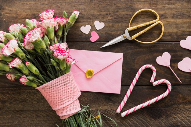 Busta vicino a bouquet di fiori con nastro, forbici e bastoncini di zucchero