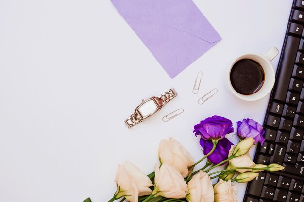 Busta viola; orologio da polso; graffetta per fogli; tazza di caffè; tastiera e fiori di eustoma su sfondo bianco