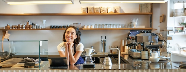 Cafe e piccola impresa sorridente barista asiatico in grembiule in piedi dietro il bancone in una caffetteria