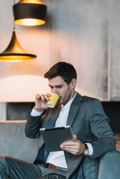 Caffè bevente del giovane uomo d&#39;affari mentre esaminando compressa digitale