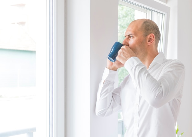 Caffè bevente dell&#39;uomo d&#39;affari che guarda attraverso la finestra dell&#39;ufficio