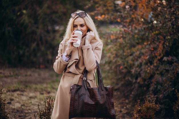 Caffè bevente della donna anziana fuori del parco di autunno