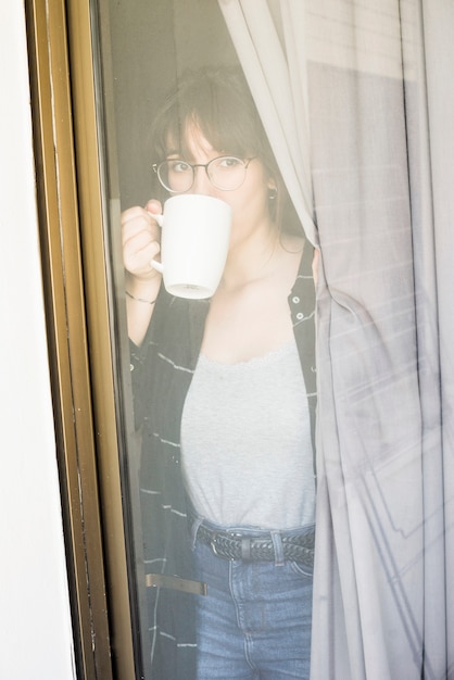 Caffè bevente della donna che guarda attraverso la finestra