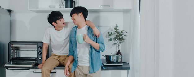 Caffè bevente delle coppie gay asiatiche, divertendosi a casa. I giovani uomini LGBTQ + che parlano felici si rilassano insieme riposano insieme il tempo romantico nella cucina moderna a casa la mattina.