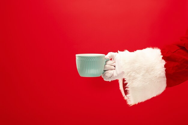 Caffè di Natale. Santa mano che tiene tazza di caffè isolato su uno sfondo rosso con spazio per il testo.