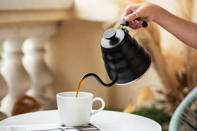 Caffè di versamento della mano di vista laterale in tazza