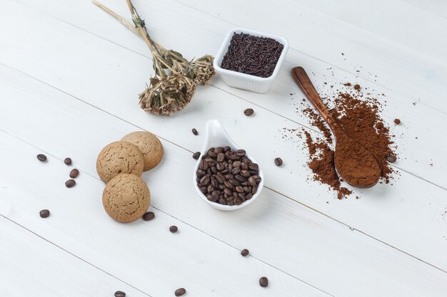 Caffè di vista di alto angolo in tazza con caffè macinato, chicchi di caffè, erbe secche, biscotti su fondo di legno. orizzontale