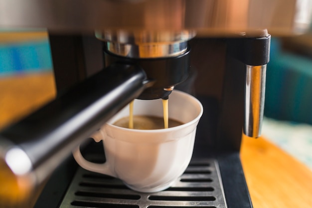 Caffè espresso caldo che versa nella tazza della porcellana