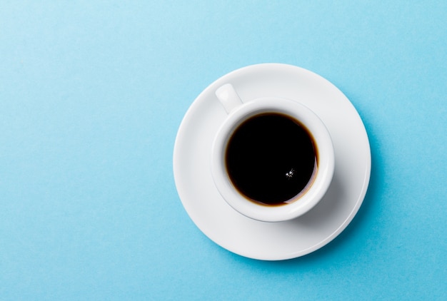 Caffè espresso classico in piccola tazza di ceramica bianca su sfondo vibrante blu.