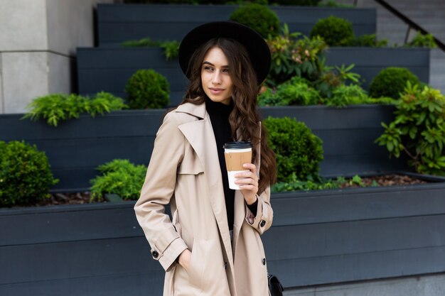 Caffè in movimento. Bella giovane donna che tiene tazza di caffè e sorridente mentre si cammina lungo la strada