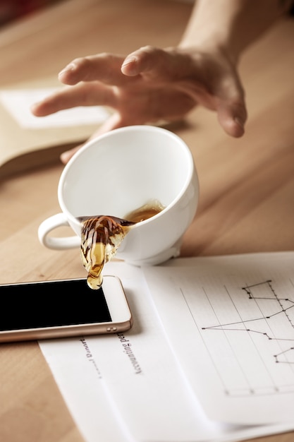 Caffè in tazza bianca che si rovescia sulla tavola di giorno lavorativo di mattina alla tavola dell'ufficio