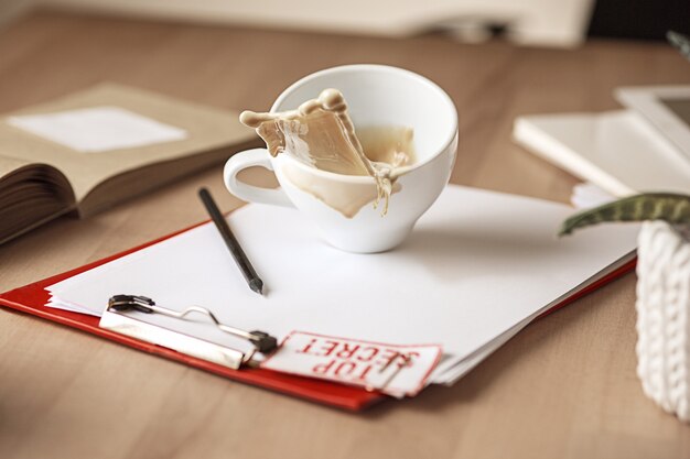 Caffè in tazza bianca che si rovescia sulla tavola di mattina alla tavola dell'ufficio