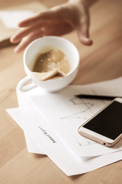 Caffè in tazza bianca che si rovescia sulla tavola di mattina alla tavola dell'ufficio