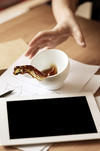 Caffè in tazza bianca che si rovescia sulla tavola di mattina alla tavola dell'ufficio