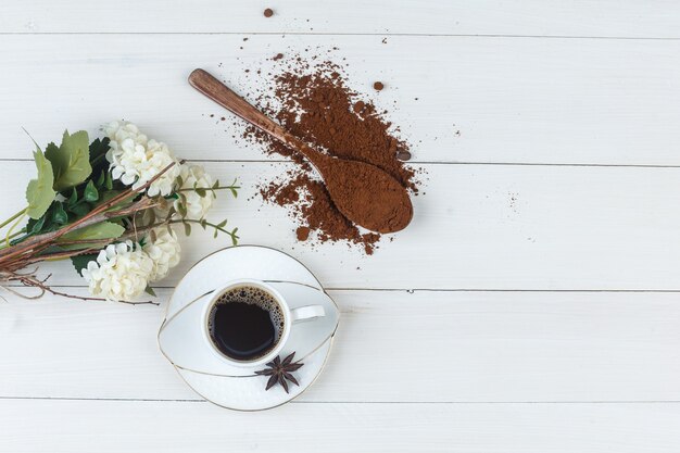 Caffè in una tazza con caffè macinato, spezie, fiori vista dall'alto su uno sfondo di legno