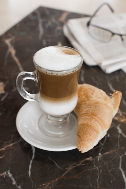 Caffè latte con cornetto e bicchieri sfocati