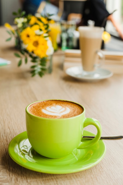 Caffè saporito del latte con arte del latte in tazza verde al ristorante