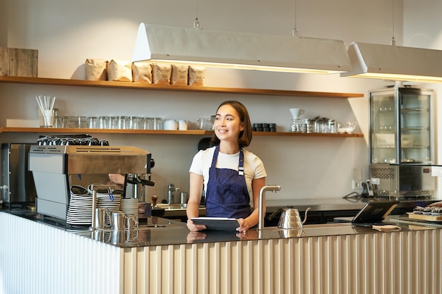 Caffetteria sorridente donna barista coreana che lavora dietro il bancone utilizzando il tablet per prendere ordini nella caffetteria