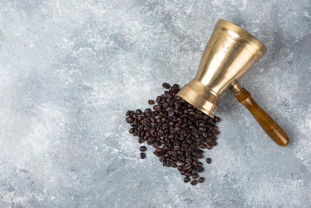 Caffettiera piena di chicchi di caffè tostati sulla superficie in marmo.