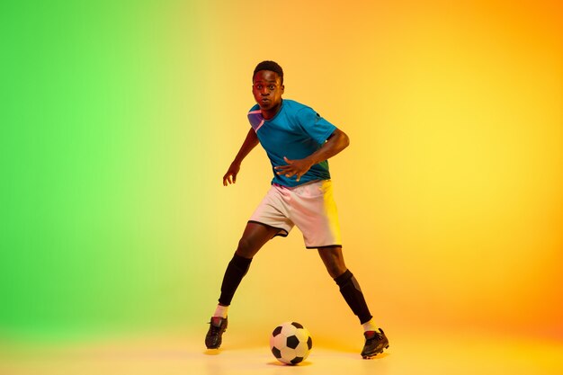 Calcio maschile, allenamento del giocatore di football in azione isolato su studio sfumato in luce al neon