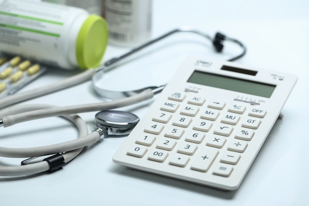 Calcolatrice, stetoscopio e bottiglie di medicina su sfondo bianco