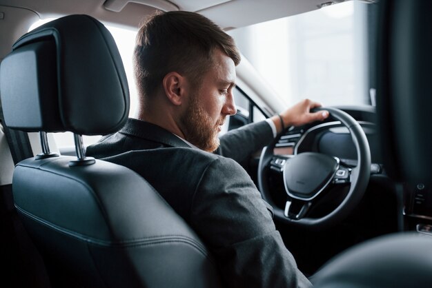 Cambio di marcia. Uomo d'affari moderno che prova la sua nuova automobile nel salone dell'automobile