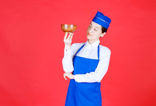 Cameriera donna in uniforme in piedi e in possesso di una ciotola di legno.